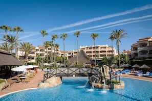 Piscina de resort com palmeiras, espreguiçadeiras e uma ponte.