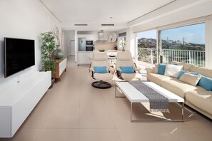 Ein modernes Wohnzimmer mit Flachbildfernseher, einer Couch, zwei Sesseln, einem Couchtisch und einem Balkon mit Blick.