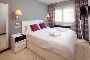 Ein Hotelzimmer mit Bett, Nachttischen, Nachttischlampen, einem Fernseher und einem Fenster mit Vorhängen.