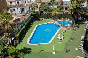 A swimming pool with a dolphin mural, surrounded by green lawn, palm trees, and lounge chairs. - Boliches Mediterraneo Real Coastal by Alfresco Stays (Fuengirola)