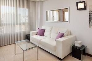 Ein modernes Wohnzimmer mit einem weißen Sofa, einem Glastisch und einem Beistelltisch mit einer Vase.