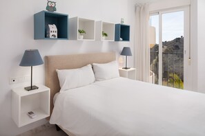 Een slaapkamer met een bed, twee nachtkastjes, een wandplank met decoratieve objecten en uitzicht door een schuifdeur.