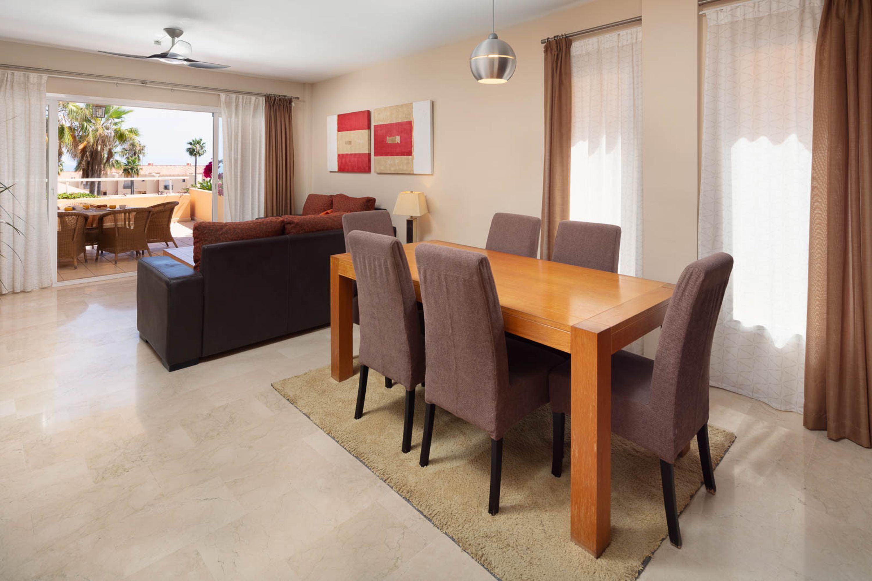 Una sala de estar moderna con una mesa de comedor, sofá y sillas, un balcón con vistas, y obras de arte en la pared.
