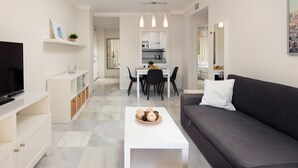 Een moderne woonkamer met een bank, salontafel, televisie en een eethoek met stoelen en een tafel.