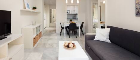 A modern living room with a sofa, a coffee table, a TV, and a dining area with chairs and a table.