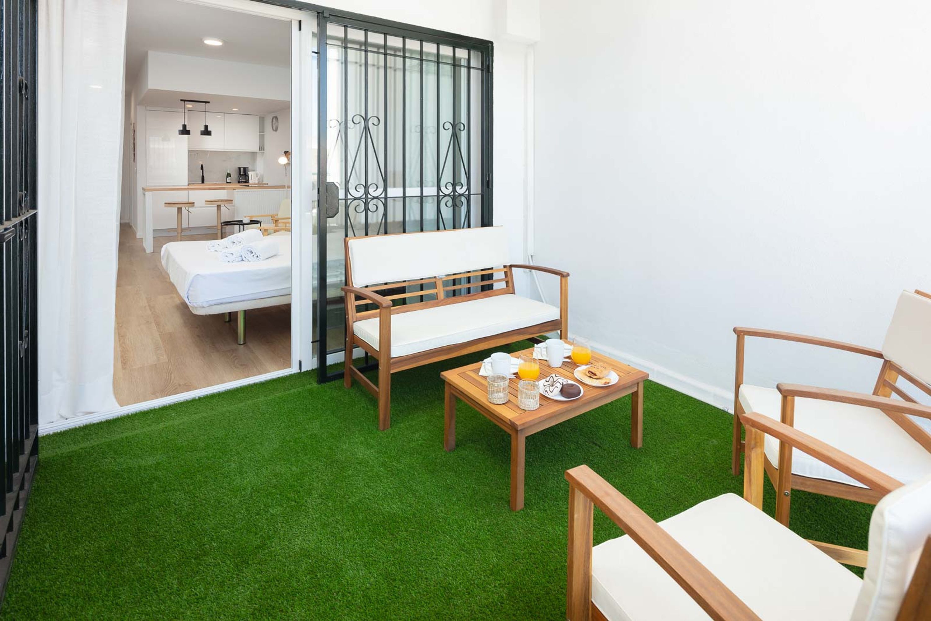A room with a bed, a wooden table with breakfast, a chair, and a view of a kitchen and bathroom through a sliding door.