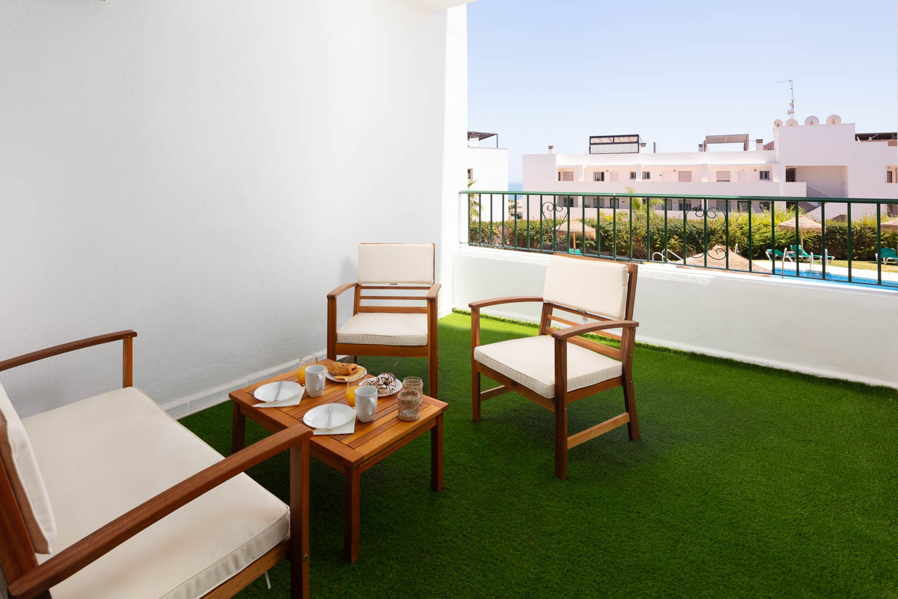 A balcony with artificial grass, wooden furniture, and a view of buildings.
