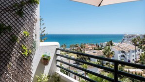 Un balcón con vistas al mar, una pared de malla con plantas y una maceta colgante.