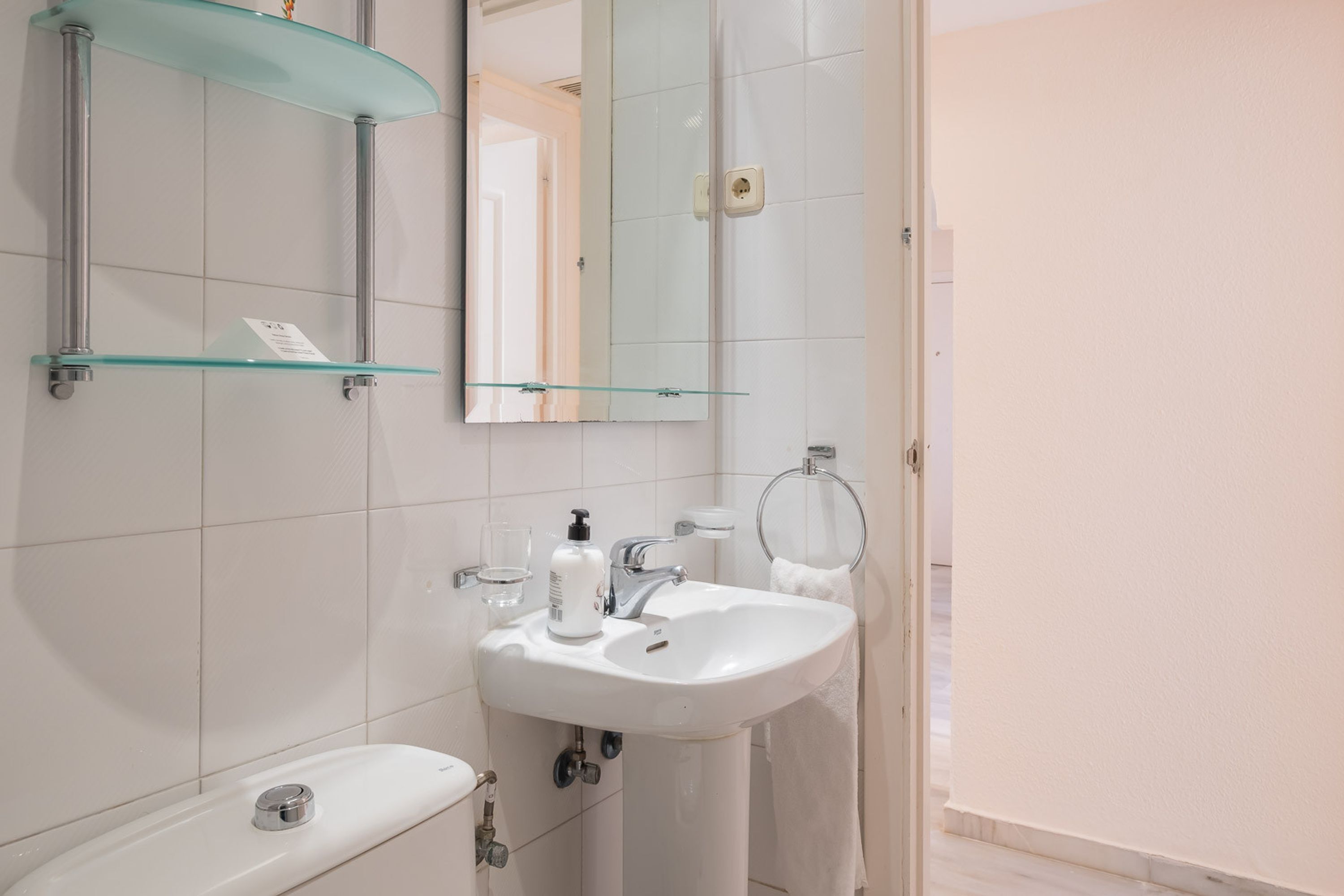 Une salle de bain avec un lavabo blanc, des étagères en verre, un miroir et un porte-serviettes.
