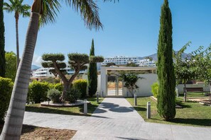 Un sendero conduce a un edificio de diseño moderno, rodeado de abundante vegetación y palmeras.