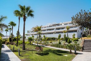 Un hotel moderno con una estructura de varios pisos, un jardín bien cuidado con palmeras y un cielo despejado.