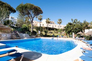 Ein Pool mit Liegestühlen, umgeben von Bäumen und Gebäuden.