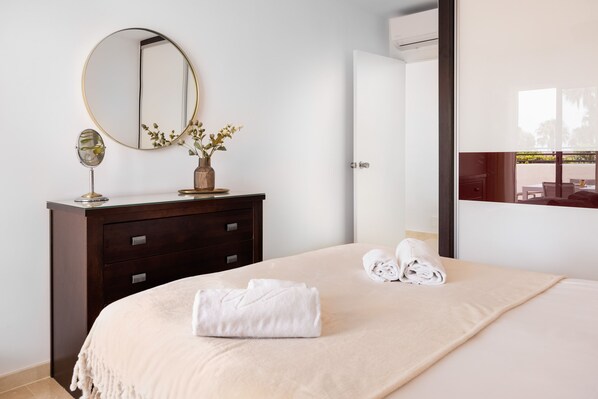Une chambre d’hôtel avec un lit, une commode dotée d’un miroir, un vase avec des fleurs et une serviette soigneusement pliée posée sur le lit.