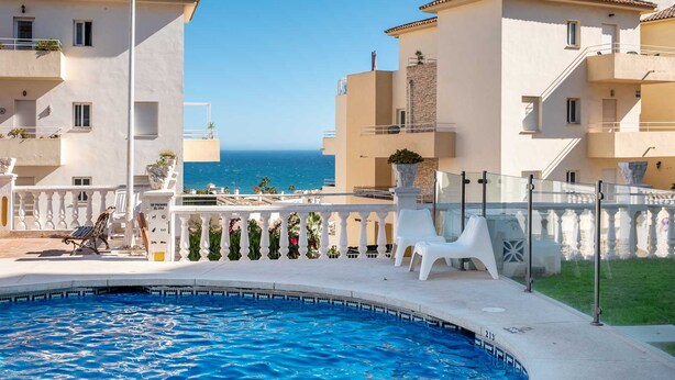 Piscina com vista para o mar, cercada por edifícios com varandas e um muro branco.