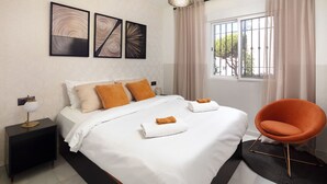 Quarto bem arrumado com cama, cadeira, mesa de cabeceira e obras de arte na parede.