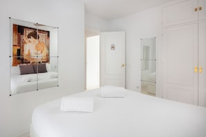 Une chambre d’hôtel avec un grand lit, un tableau au mur, une porte ornée d’un petit emblème et un miroir.