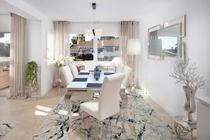 Un comedor moderno con una mesa para cuatro, sillas blancas, un tapete estampado y vista a un edificio con tejado de tejas.