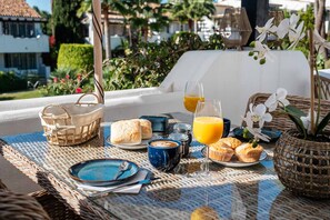 Un desayuno con cestas de mimbre, platos, una taza de café, muffins y un vaso de jugo de naranja sobre una mesa.