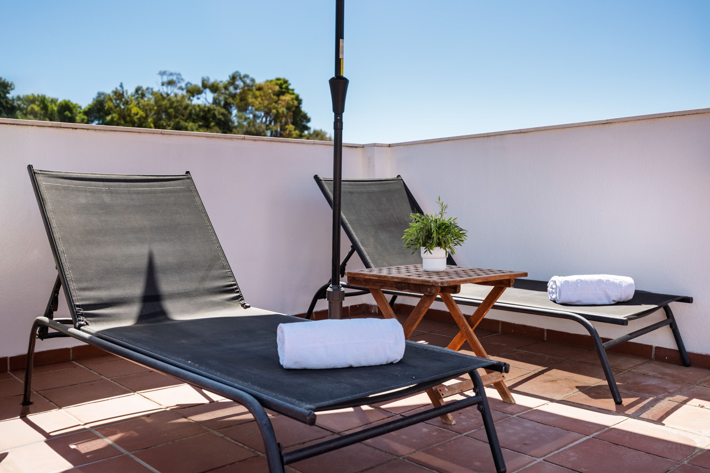 Two lounge chairs with towels, a small table with a plant, and a metal pole.