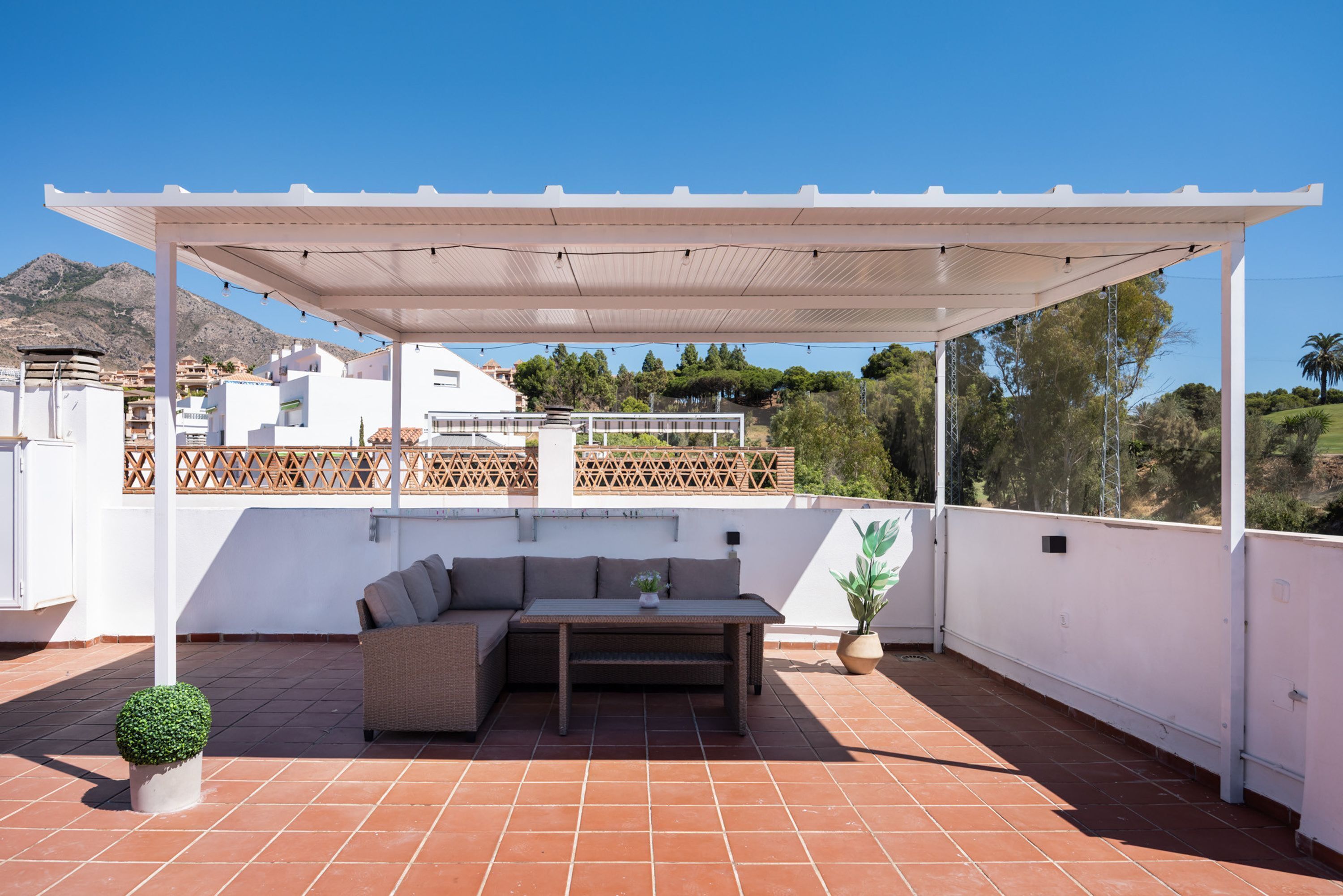A covered outdoor seating area with a sofa, table, and potted plants.