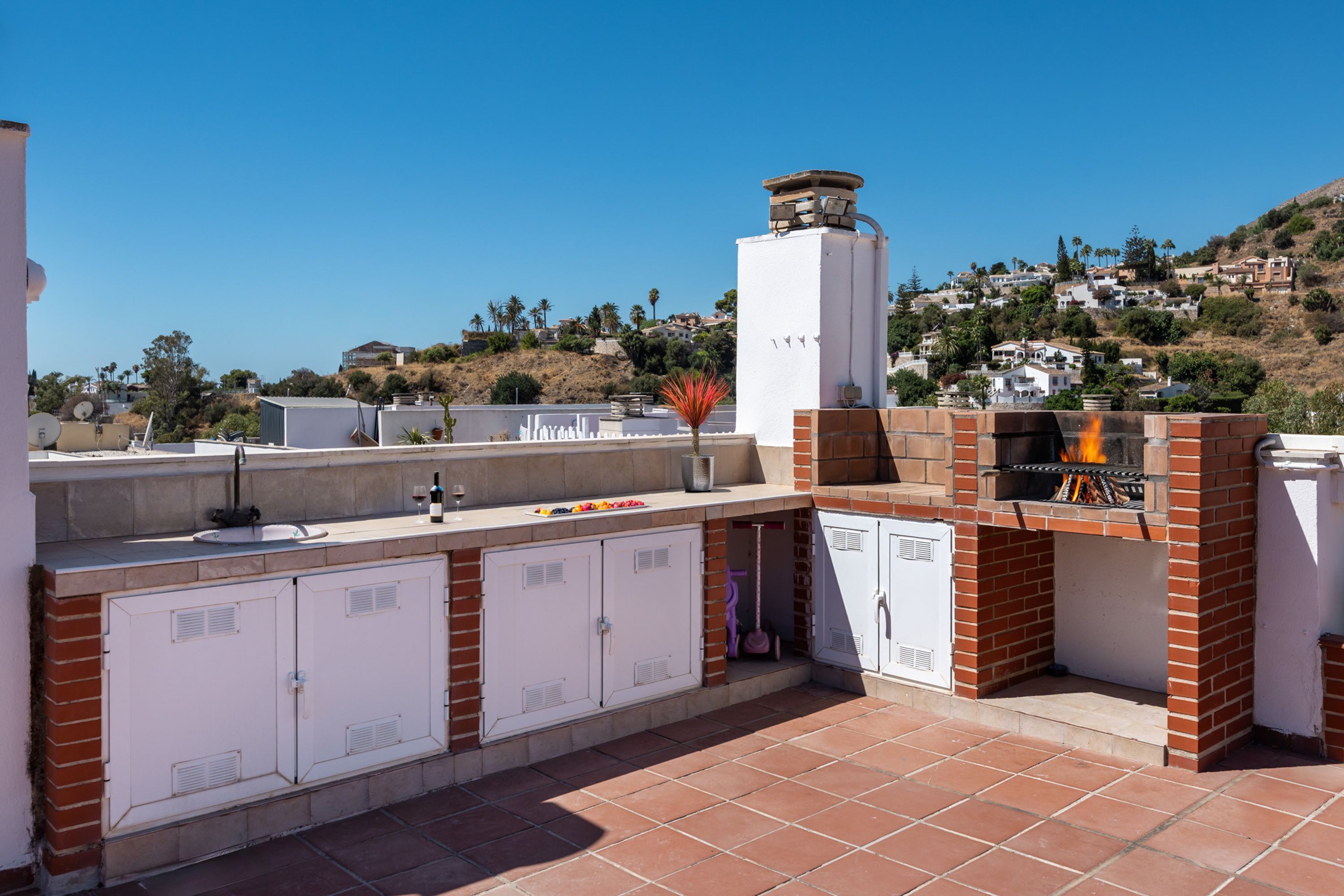 Un espace cuisine extérieur comprenant un barbecue, des placards de rangement et une vue sur un quartier situé sur une colline.