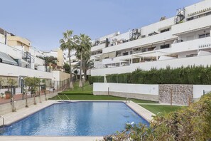 Zona residencial con piscina, edificios blancos y una palmera.