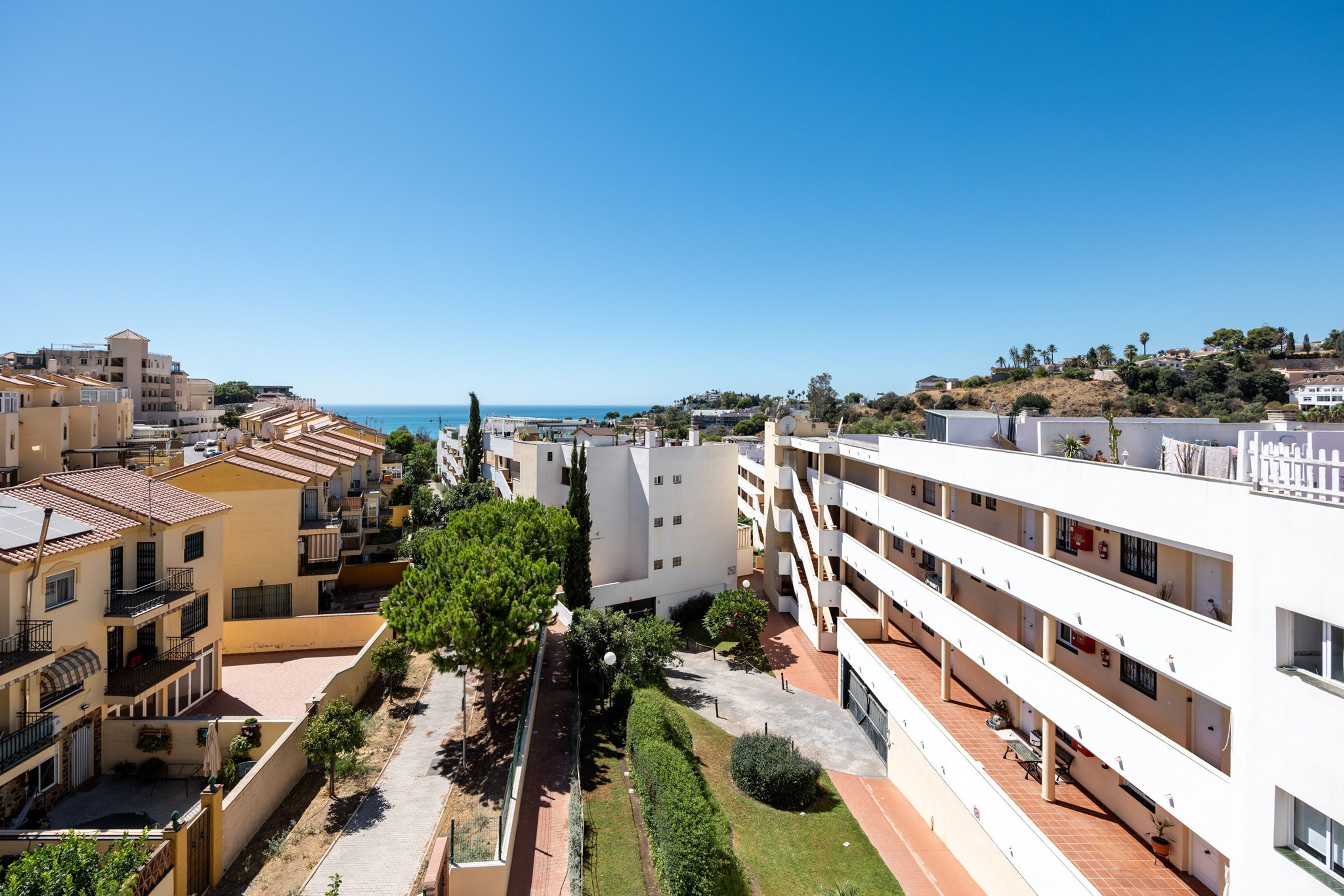 A residential area with multi-story buildings, a clear sky, and a distant view of the sea.