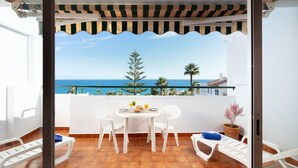 Un balcón con una mesa y sillas blancas, vista al mar y una planta en maceta.