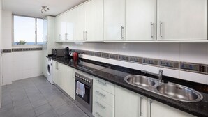 Una cocina moderna con gabinetes blancos, lavamanos de acero inoxidable, horno empotrado y lavadora.