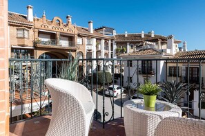 A balcony with wicker furniture, a green potted plant, and a view of traditional buildings with balconies. - AS EXT Mijas Puebla Aida 12L (Mijas)