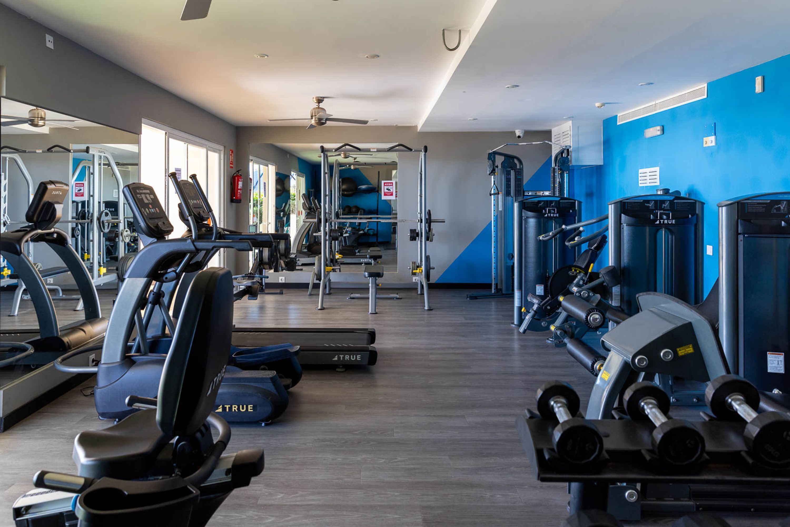 Un gimnasio con cintas de correr, máquinas de pesas y pesas sueltas.