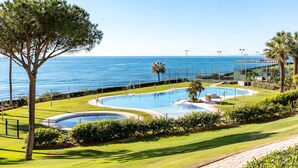 A pool area with multiple swimming pools, a palm tree, and a view of the sea. - AS EXT CBP Granados 1201 (Mijas)