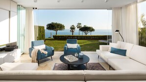 A modern living room with a white sofa, blue armchairs, a coffee table, and a view of the sea. - AS EXT CBP Granados 1201 (Mijas)