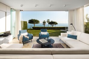 Una sala de estar moderna con un sofá blanco, sillones azules, una mesa de centro y vista al mar.