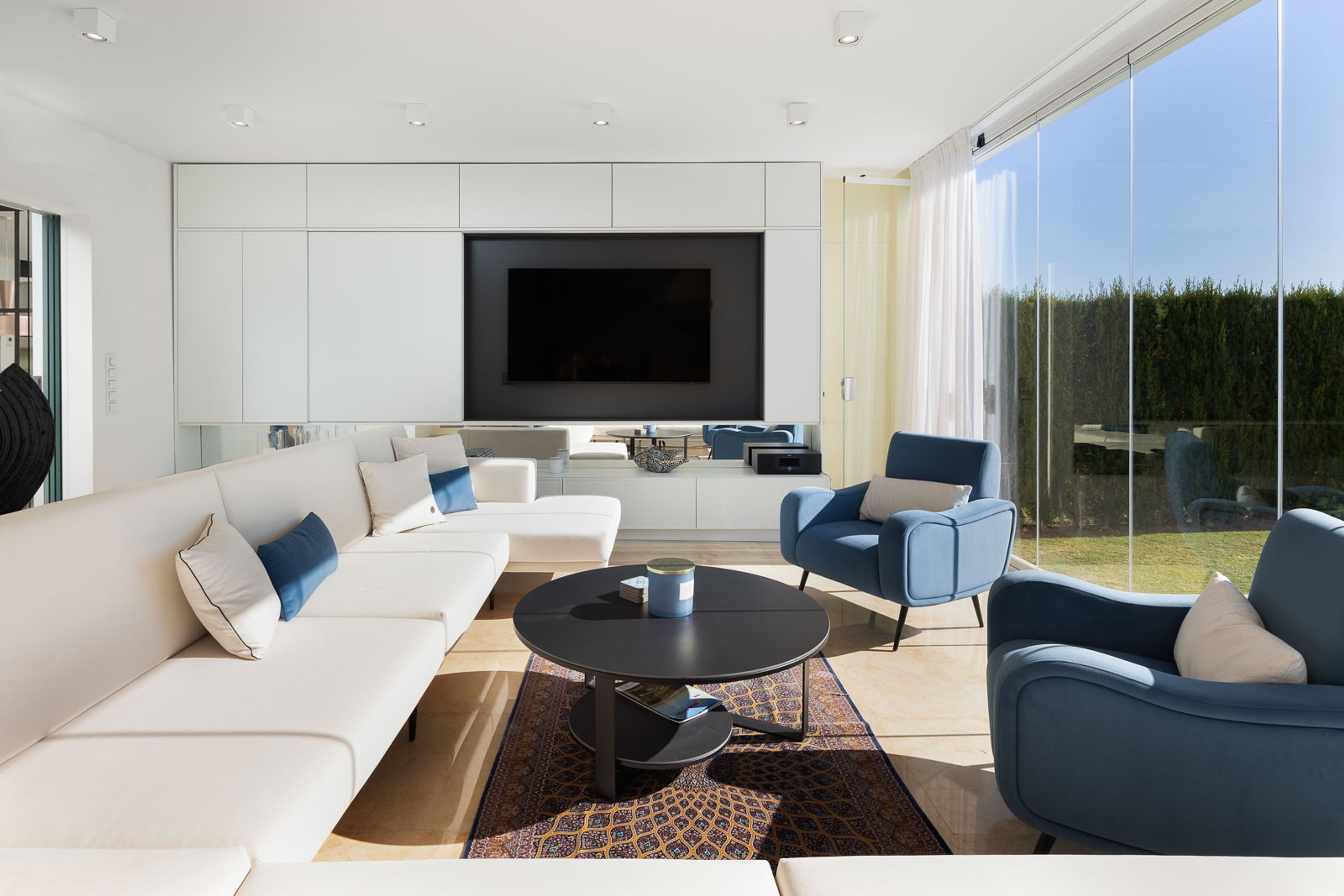 Un salon moderne doté d’un grand téléviseur à écran plat, de canapés blancs, de fauteuils bleus et d’une table basse.