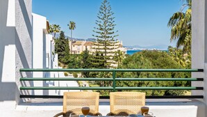 A balcony with wicker chairs, a table with a white tablecloth, and a view of a coastal area with buildings and trees. - AS MD 5D3 in Mijas Costa (Mijas)