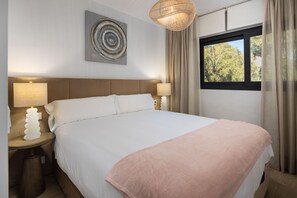 A neatly made bed with a white and pink blanket, two bedside lamps, a wall art piece, and a window with curtains. - AS EXT Estp ONE 80 Suites 211a (Estepona)