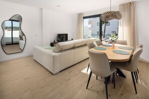 A modern living room with a sofa, dining table, chairs, a TV, and a large window. - AS EXT Estp ONE 80 Suites 211a (Estepona)