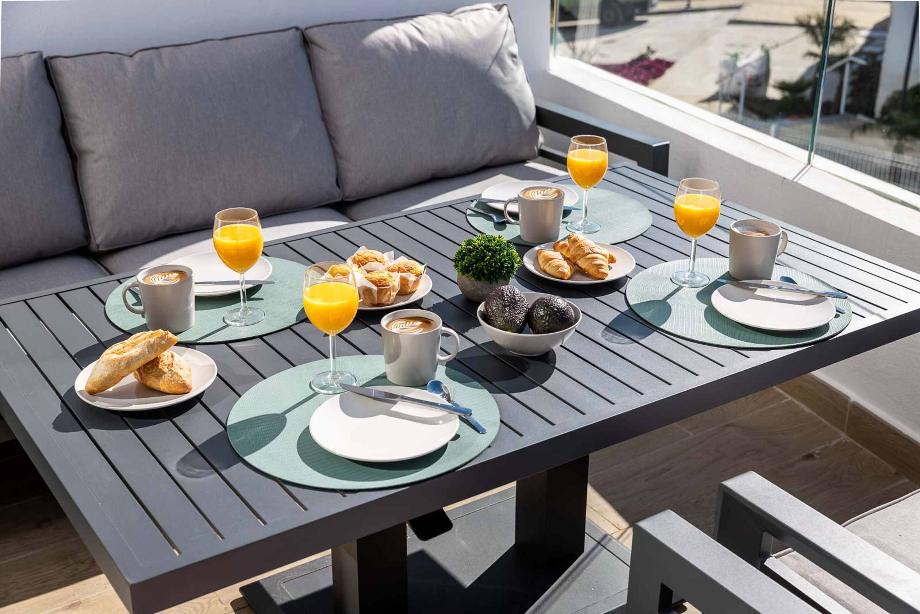 Ein Frühstückstisch mit Tellern, Croissants, Kaffee und Orangensaft auf einem Balkon.