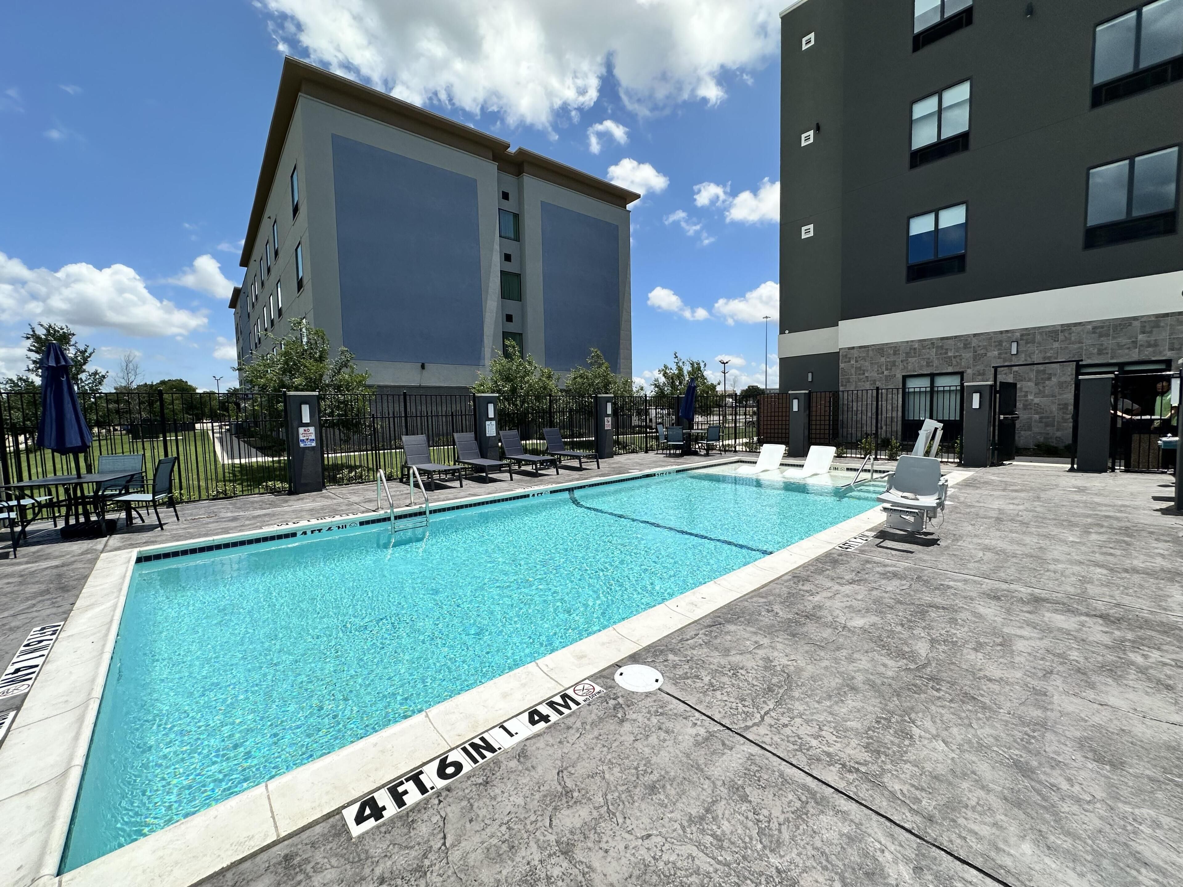A swimming pool with a 4ft.6in.1.4m depth, surrounded by lounge chairs and a table, with buildings in the background.