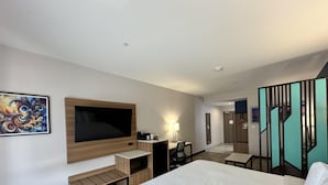 Habitación de hotel con una cama, televisión, escritorio, silla, lámpara y un cuadro en la pared.
