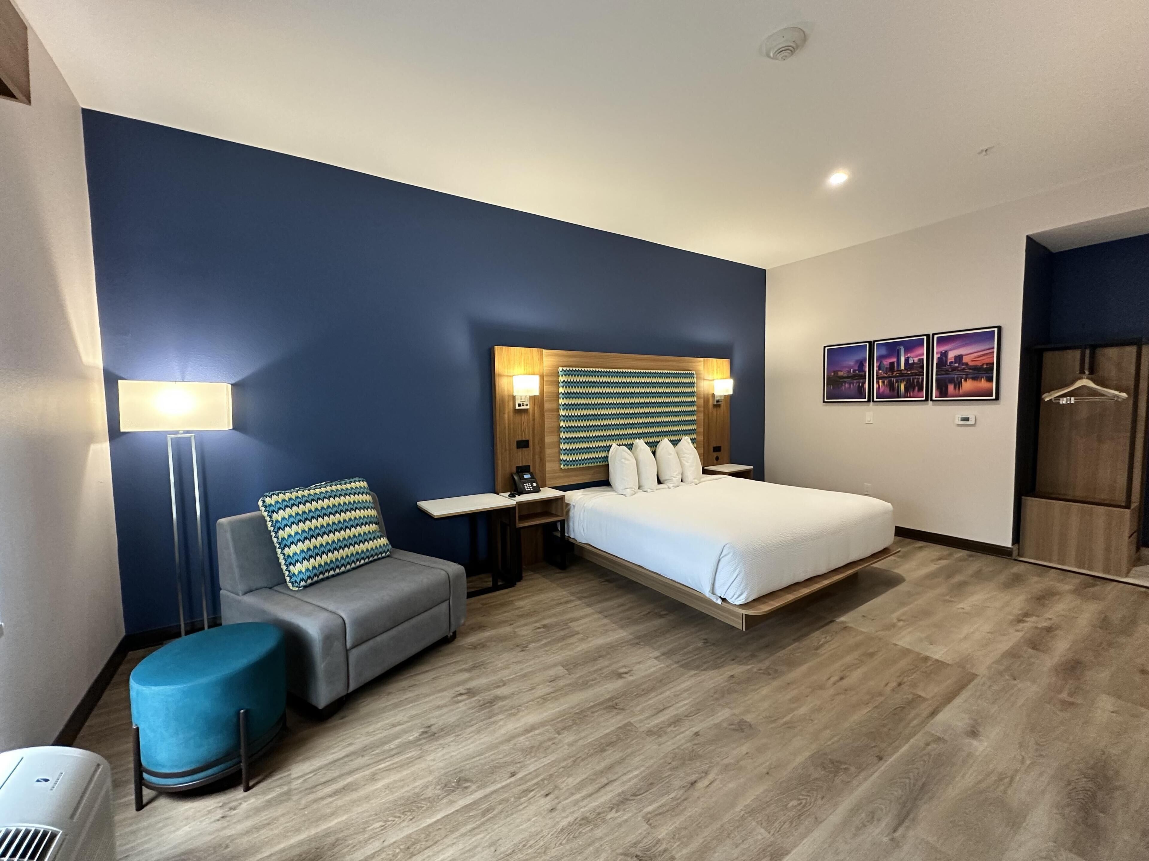 Habitación de hotel con cama, mesita de noche, lámpara y una pequeña zona de estar.