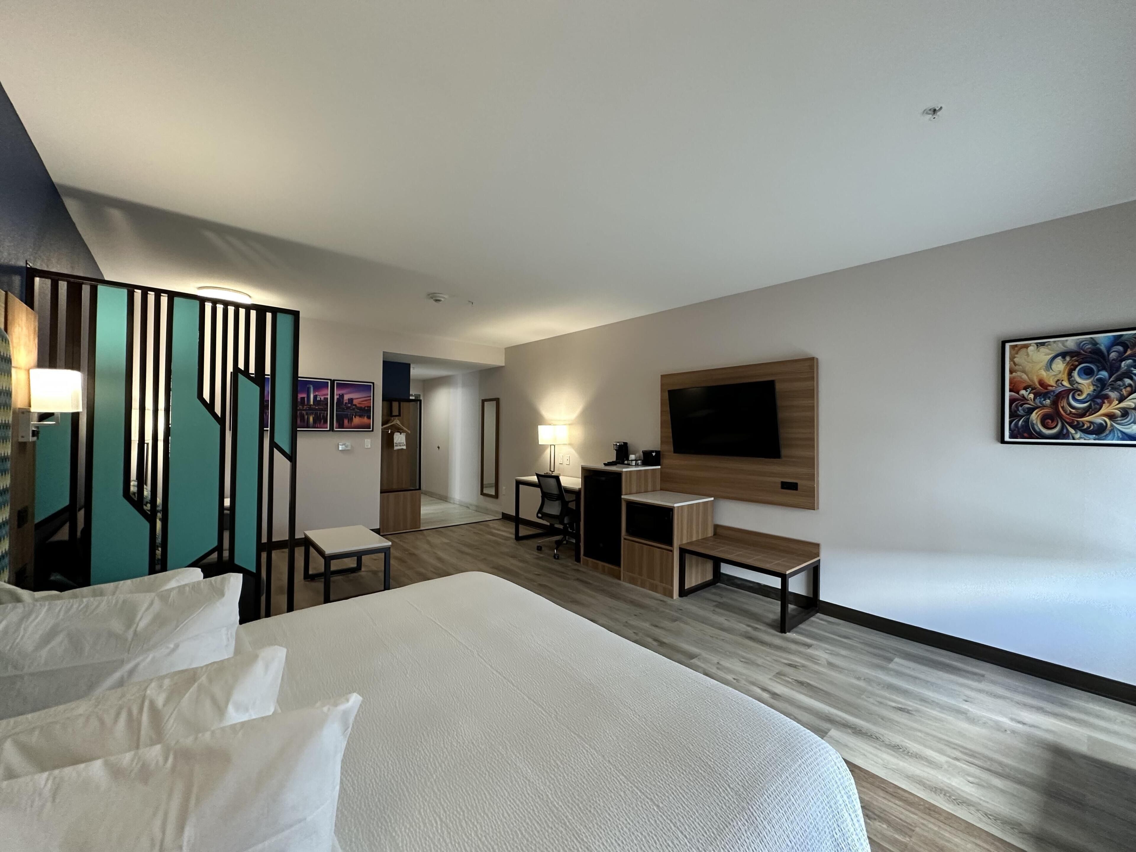 A hotel room with a bed, desk, chair, TV, and artwork.