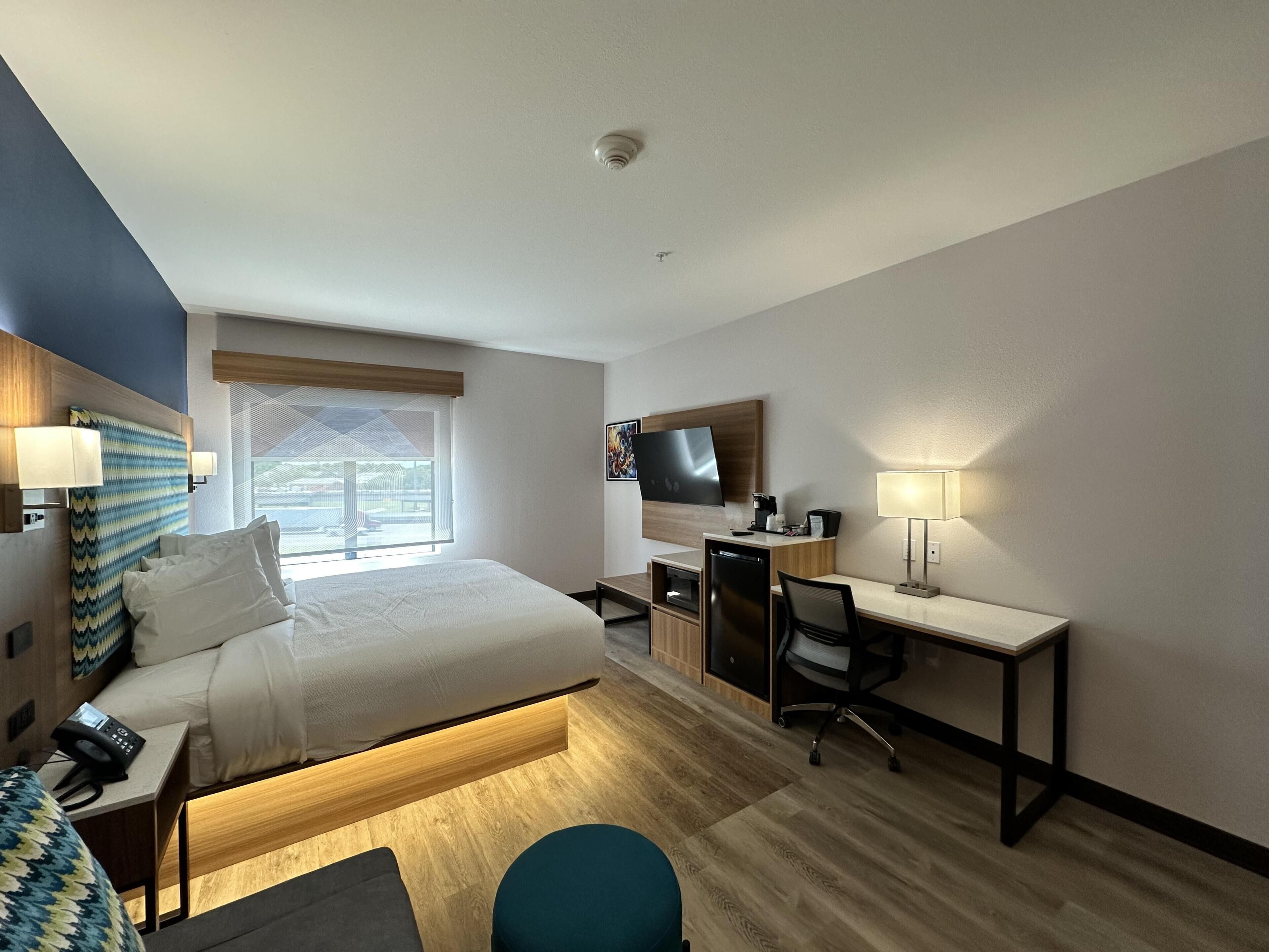 Habitación de hotel con cama, escritorio, silla, televisión y ventana.