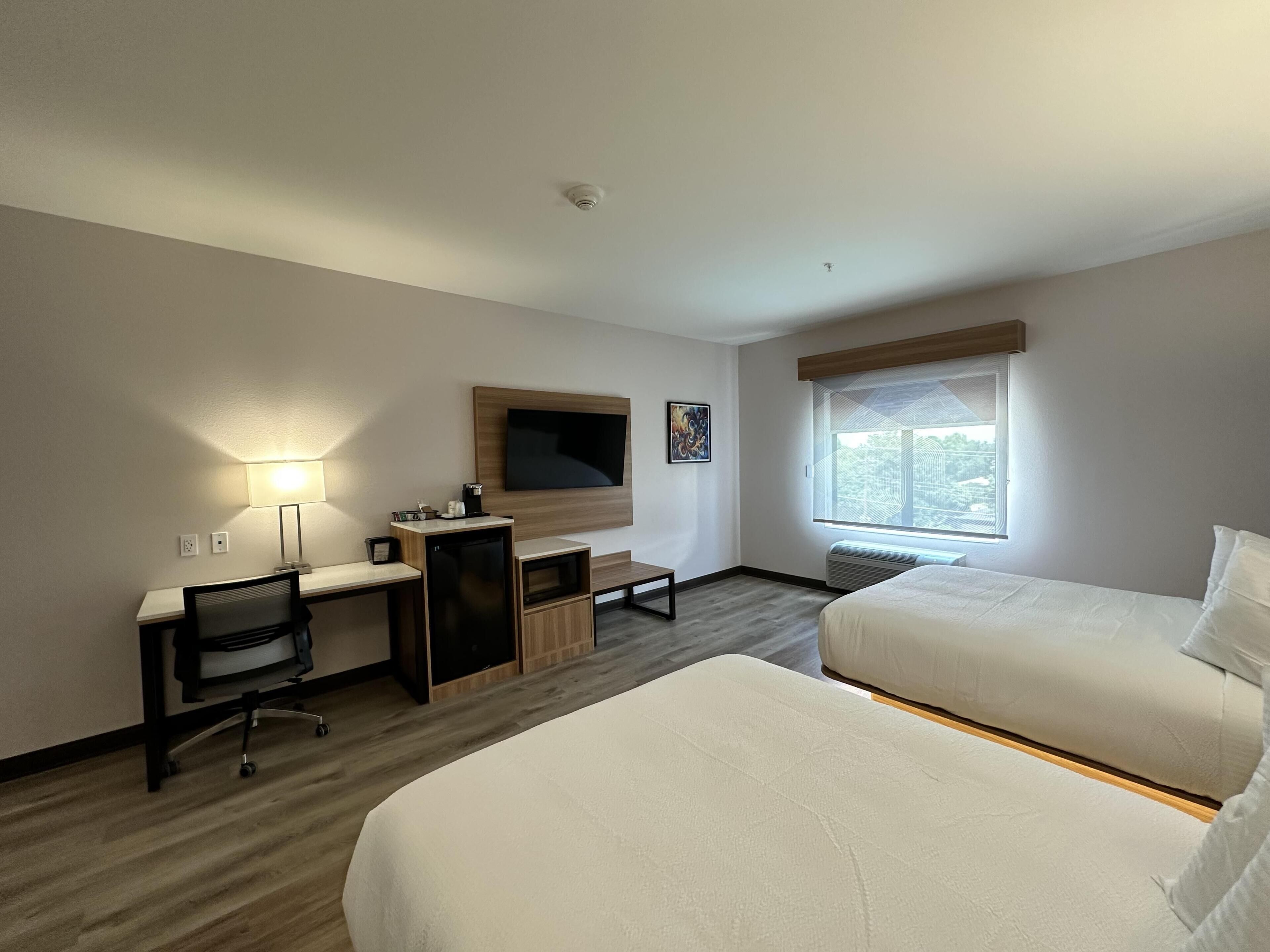 Een hotelkamer met een bureau, stoel, televisie, twee bedden en een raam.