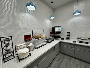 Un área de desayuno moderna con estación de autoservicio, exhibición de pastelería y máquina de café.