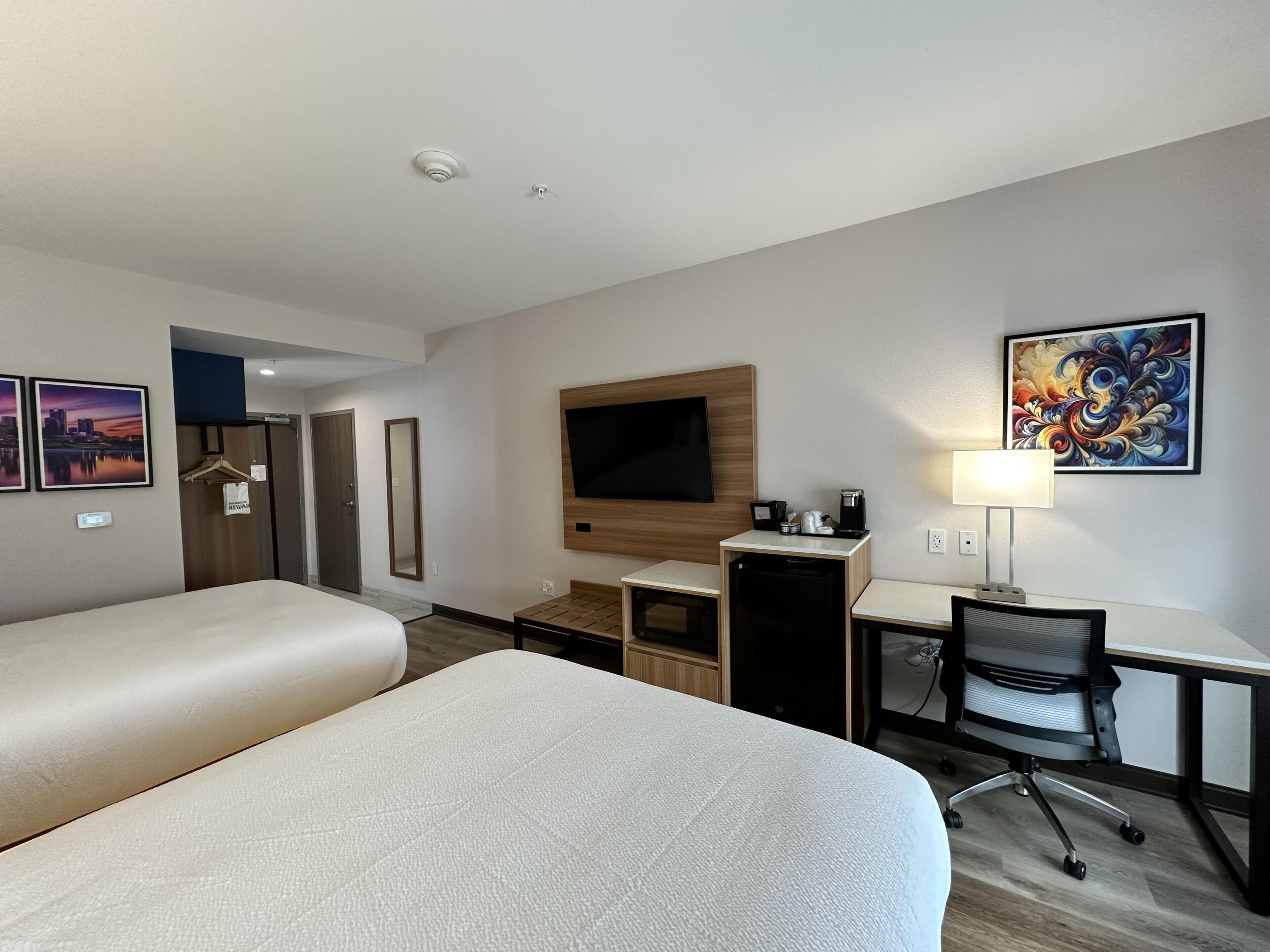 Habitació d'hotel amb dos llits, una taula, una cadira, un televisor, una cafetera i obres d'art a les parets.