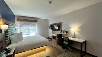 A hotel room with a bed, desk, chair, TV, and a window.