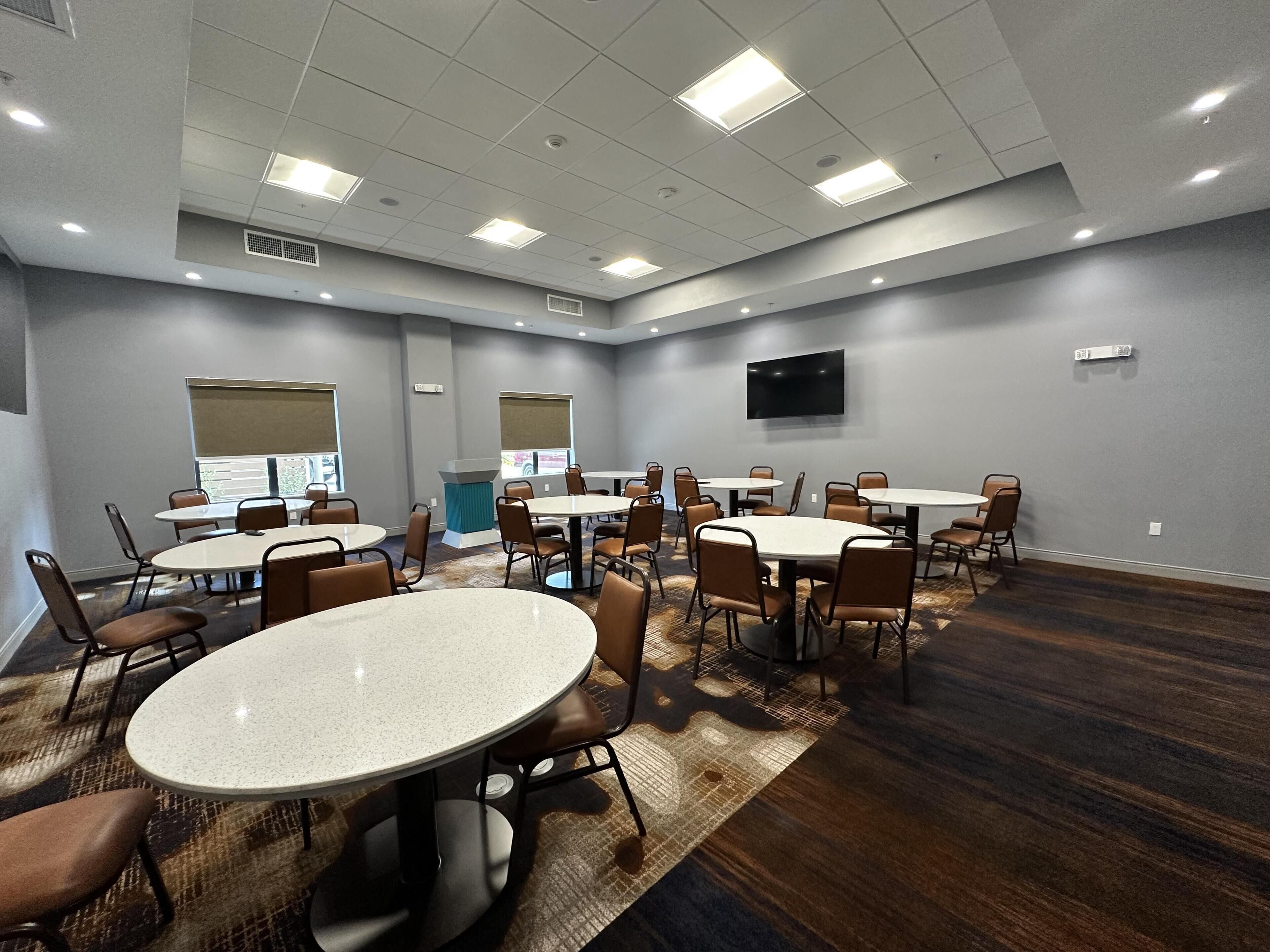 A conference room with multiple tables and chairs, a flat-screen TV mounted on the wall, and a patterned carpet.