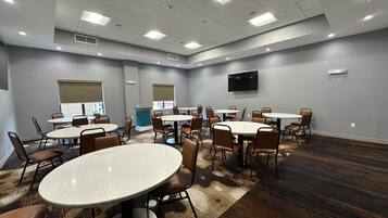 A conference room with multiple tables and chairs, a flat-screen TV mounted on the wall, and a patterned carpet.